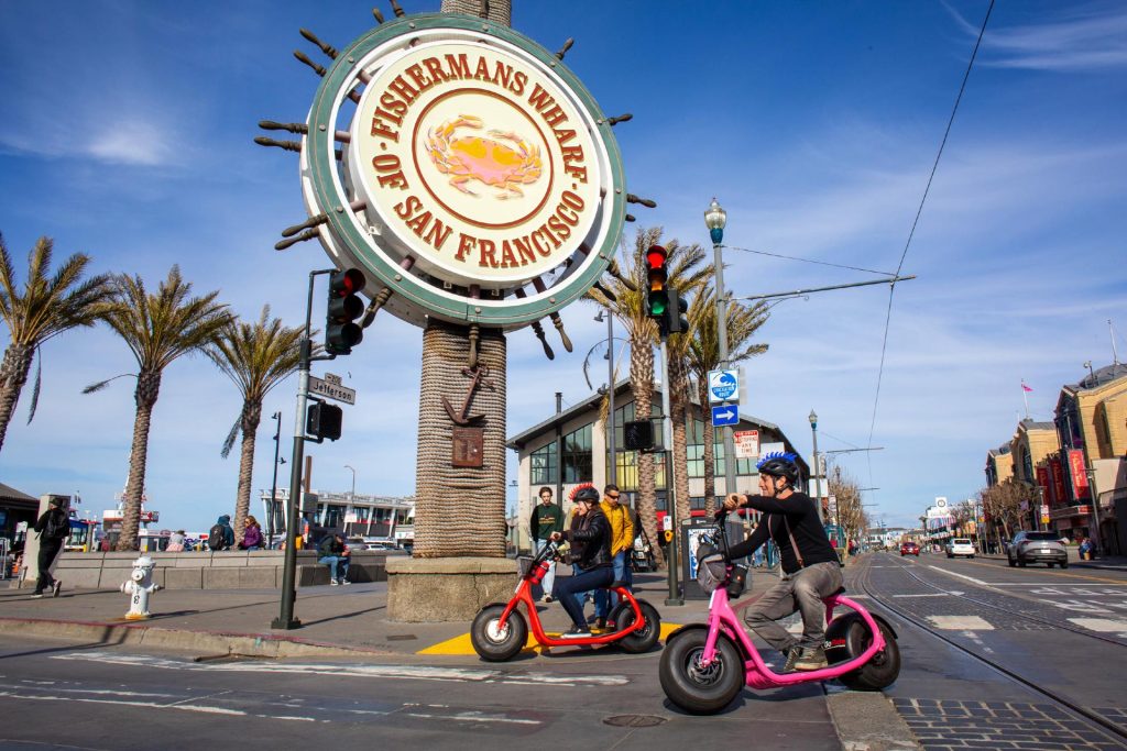 Electric Scooter Rentals ride past the iconic Fishermans Wharf Sign - Rent an E-scooter with fully guided GPS GoRide tour to the Golden Gate Bridge - departs from Umbrella Alley